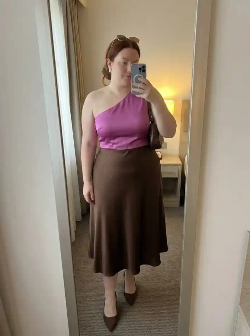 Magenta one-shoulder fitted top tucked into chocolate brown satin midi skirt with brown pumps