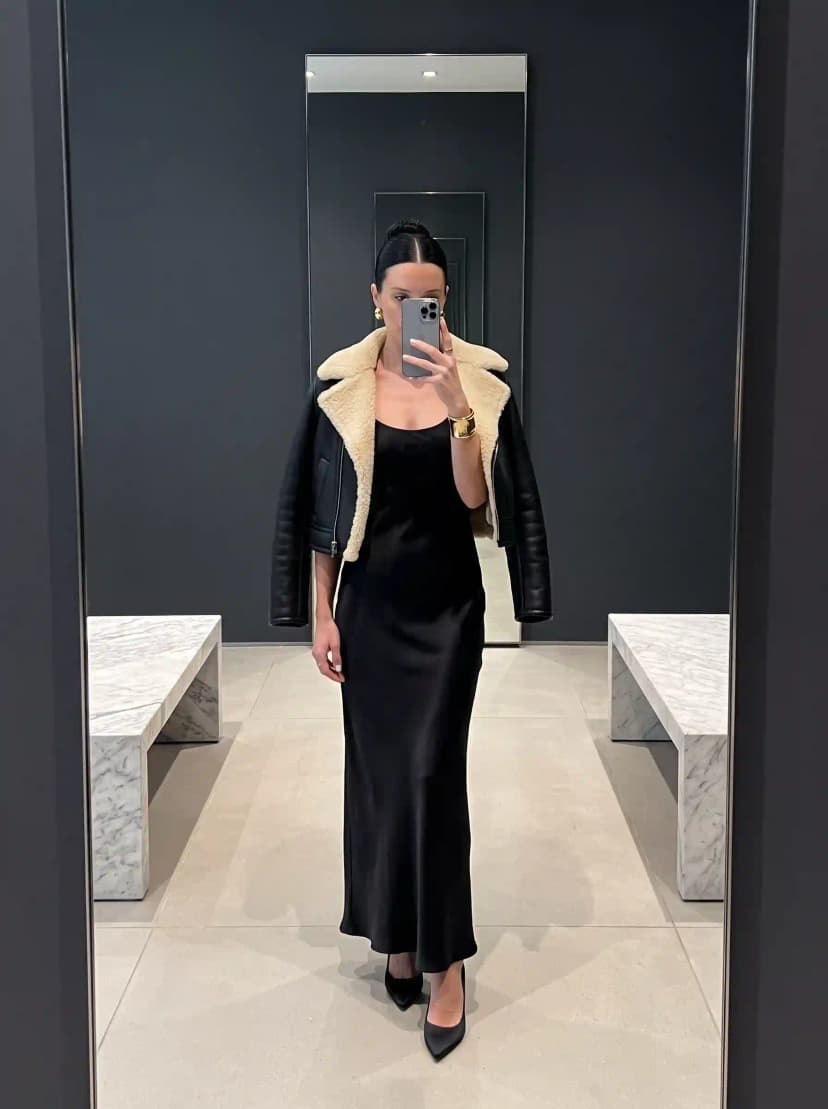 Black leather shearling aviator jacket, black satin slip dress, and black pumps